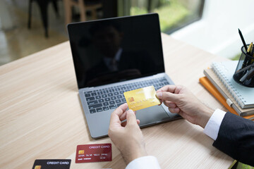A man is using a laptop and a cell phone to pay for something. He is holding a credit card and a debit card
