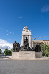 Obraz premium The Tisza Istvan Memorial in Budapest features bronze sculptures and a central statue, set against a blue sky with a crane and historic building visible.