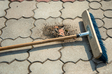 A broom is placed on a paved pathway where dirt and small debris are visible, indicating recent...