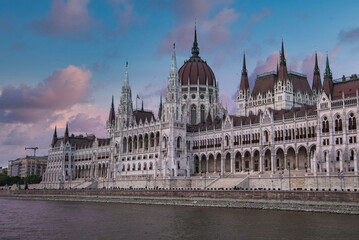 Obraz premium The neo Gothic Hungarian Parliament Building in Budapest, Hungary, with spires and domes, reflected on the Danube River under a pink and blue sky.