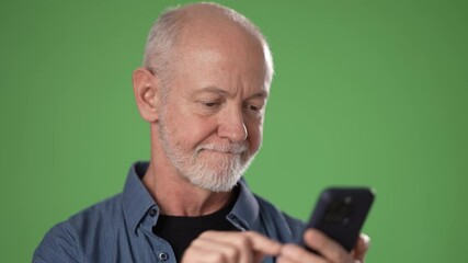 A mature man with gray hair and a beard focuses attentively on his smartphone, set against a vibrant green screen backdrop, likely for a project or presentation. - Powered by Adobe