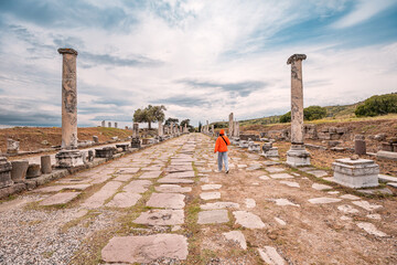 Tourist walking through the ancient Roman road in Pergamon, Turkey, surrounded by ruins and columns, exploring the historical site