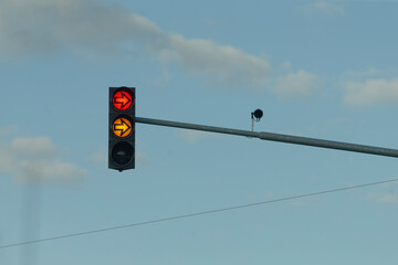 A traffic light prominently displaying red and yellow colors stands against a clear blue sky, emphasizing the importance of traffic control and ensuring road safety for all. Its vital