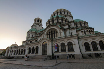 Fototapeta premium Alexander Nevsky Cathedral in Sofia captured from a low angle at sunset, highlighting its majestic Neo-Byzantine architecture with green domes and intricate stone facade.