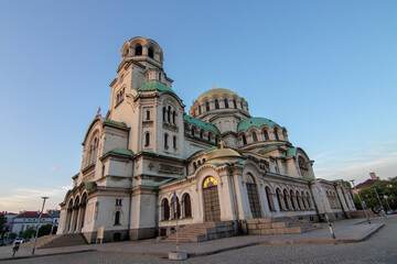 Obraz premium Wide-angle shot of Alexander Nevsky Cathedral in Sofia during golden hour, showcasing its stunning Neo-Byzantine architecture with green domes and detailed stone facade under a clear sky.