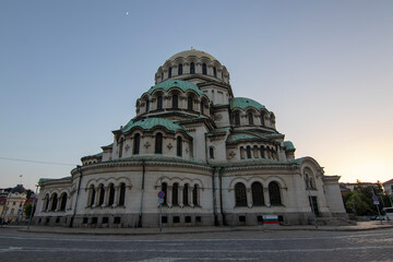 Fototapeta premium Alexander Nevsky Cathedral in Sofia captured at sunset, highlighting its grand Neo-Byzantine architecture, detailed stone facade, and iconic green domes under a soft evening sky.