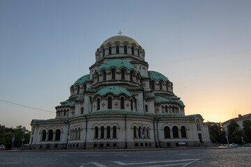 Obraz premium Alexander Nevsky Cathedral in Sofia at sunset with a clear sky, displaying its impressive Neo-Byzantine architecture, detailed stone facade, and iconic green domes in soft evening light.