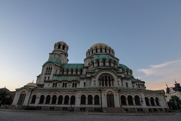 Fototapeta premium Front view of Alexander Nevsky Cathedral in Sofia at dusk, displaying its majestic Neo-Byzantine architecture, green domes, and intricate facade under a colorful evening sky.