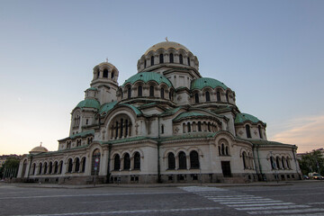 Obraz premium Wide-angle view of Alexander Nevsky Cathedral in Sofia at sunset, highlighting its grand Neo-Byzantine architecture, green domes, and detailed stone facade under a colorful sky.