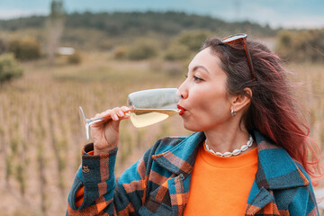 Woman enjoying a glass of white wine while tasting grapes in a sunlit vineyard, embracing the beauty of a peaceful autumn day