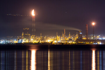 Nighttime view of İzmit Tüpraş oil refinery with glowing lights reflecting on water, chimneys...