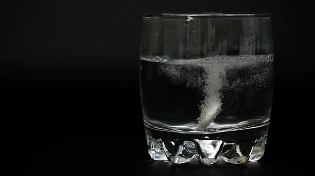 Effervescent Tablet Dissolving in Glass of Water A close-up shot of a white effervescent tablet vigorously dissolving in a clear glass of water, creating numerous bubbles against a dark background