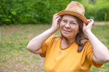 Confident Happy mature woman in yellow outfit, smiling gently, with hat, in mustard clothing outdoors, summer or spring, fashion over 50, older generation, casual style