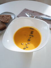 A plate of pumpkin soup with seeds and bread on the table.