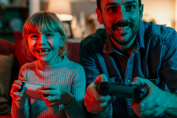 Father and daughter having fun playing videogames at home © La Famiglia