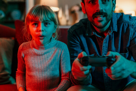 Father and daughter playing videogames at home with dramatic lighting