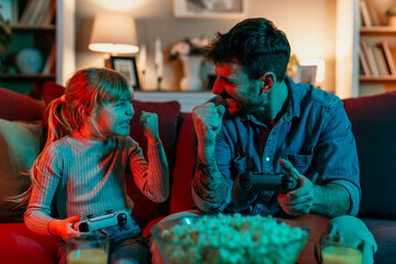 Father and daughter playing videogames exulting with joypads and popcorn