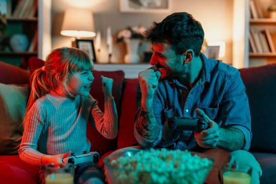 Father and daughter celebrating winning a videogame on the sofa at home