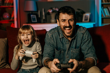 Father and daughter having fun playing videogames at home