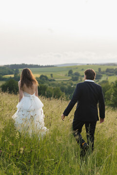 Bride and groom walking hand in hand through a green meadow during an outdoor countryside wedding.