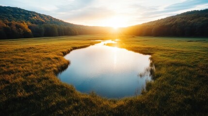 Obraz premium A stunning landscape view showcasing a tranquil lake reflecting the golden hues of sunset, surrounded by grassy meadows and distant hills, embodying natural beauty and peace.