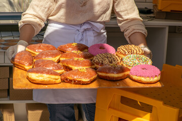 Person holding a wooden tray with assorted glazed donuts at a bakery