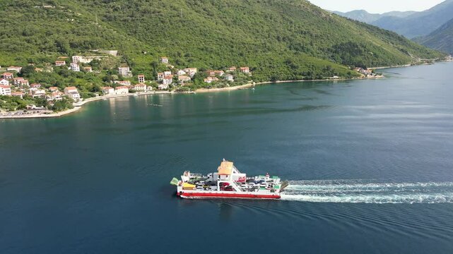 Aerial view of a passenger ferry sailing along the Verige Strait in the Bay of Kotor against the backdrop of a picturesque mountainous coastline on a sunny summer day