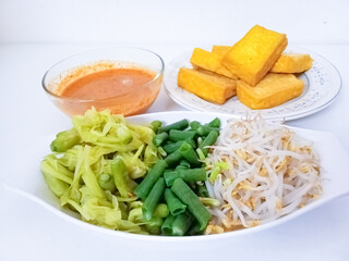 Pecel sayur or mixed steamed vegetables with peanut sauce. Traditional food from Central Java or East Java, Indonesia. Along with Tahu kuning (yellow tofu). Suitable for breakfast menu. In white table