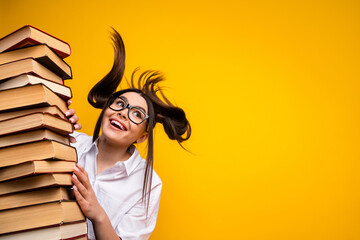 Excited student with stacks of book posing against a bright yellow background emphasizing education...