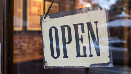 A vintage-style "Open" sign hangs in a shop window, indicating the business is currently welcoming customers.