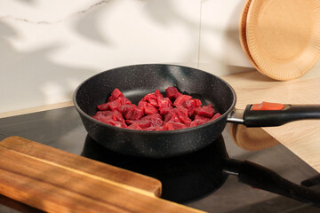 Cooking beef cubes in a modern kitchen on a stovetop with wooden utensils nearby