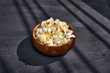 A wooden bowl filled with fluffy popcorn sits on a textured surface
