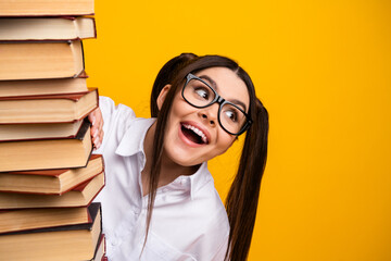 Playful young student with a stack of book on yellow background emphasizing education and...