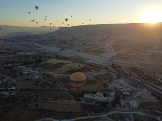 A magical drone shot of sunrise over G&ouml;reme as colorful hot air balloons lift off, painting the sky above the surreal Cappadocian landscape in golden light.