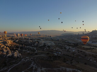 A magical drone shot of sunrise over G&ouml;reme as colorful hot air balloons lift off, painting the sky above the surreal Cappadocian landscape in golden light.