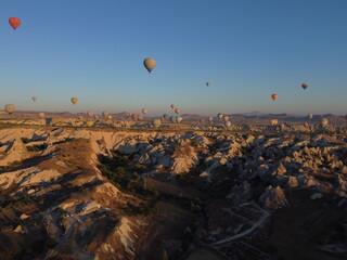 A magical drone shot of sunrise over Göreme as colorful hot air balloons lift off, painting the sky above the surreal Cappadocian landscape in golden light.