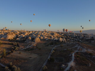 A magical drone shot of sunrise over G&ouml;reme as colorful hot air balloons lift off, painting the sky above the surreal Cappadocian landscape in golden light.