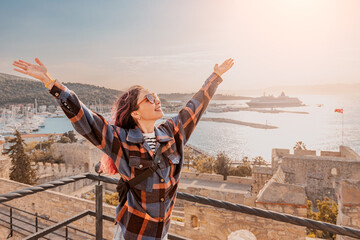 Young woman opening arms, enjoying freedom and amazing view of Turkish city Cesme, Aegean sea and cruise ship from medieval Castle