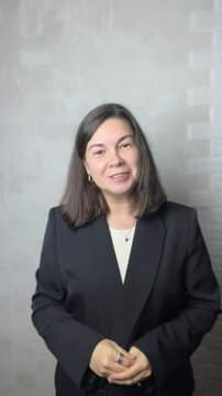 woman talking head video in black jacket indoors on light wall background
