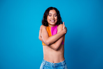 Fototapeta na wymiar Young woman expressing self care and confidence wearing trendy casual outfit against vibrant blue background