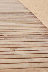Wooden decking on the beach, close-up on the boards. Boardwalk. Background. Weathered wooden boards with scattered sand, summer warm lighting. Selective focus