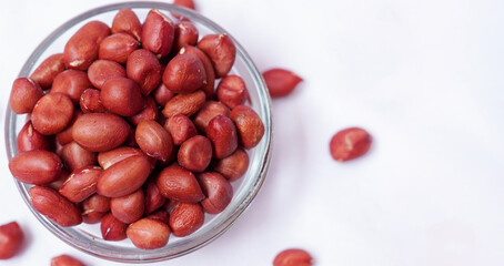 Raw red peanuts spilling from a glass bowl on white background. Healthy snack and organic food concept.