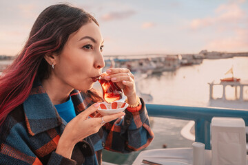 Tourist enjoying a cup of traditional tea with a beautiful sunset over a turkish marina in the background