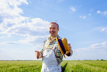 Portrait of joyful farmer standing in green wheat field looking at camera.