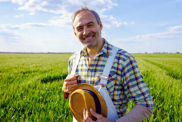 Portrait of adult male farmer standing in green wheat field looking at camera.