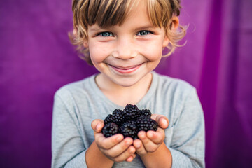 Adorable kid holding blueberry fruit and smiling over violet studio background. Healthy relationship with food and child nutrition concept. Healthy baby food with vitamins and kids vegetarianism