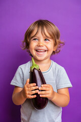 Adorable kid holding eggplant vegetable and smiling over violet studio background. Healthy relationship with food and child nutrition concept. Healthy baby food with vitamins and kids vegetarianism