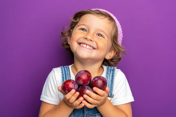Adorable kid holding plums fruits and smiling over violet studio background. Healthy relationship with food and child nutrition concept. Healthy baby food with vitamins and kids vegetarianism