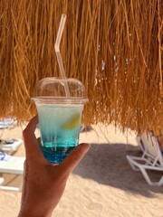 Cold Blue Lagoon cocktail with a straw parasol and a blurry beach in the background