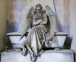 Old angel statue sitting on a tomb in contemplation. Memory and nostalgia.